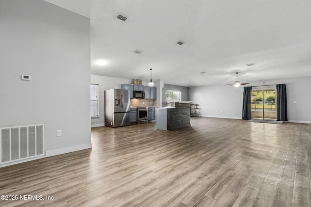 unfurnished living room featuring wood finished floors, a wealth of natural light, ceiling fan, and visible vents