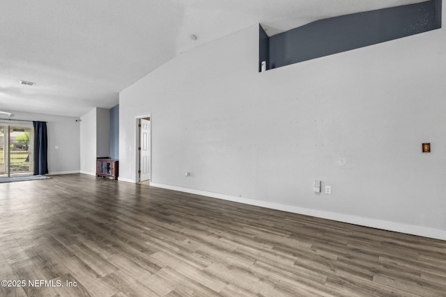 unfurnished living room featuring wood finished floors, baseboards, lofted ceiling, and visible vents