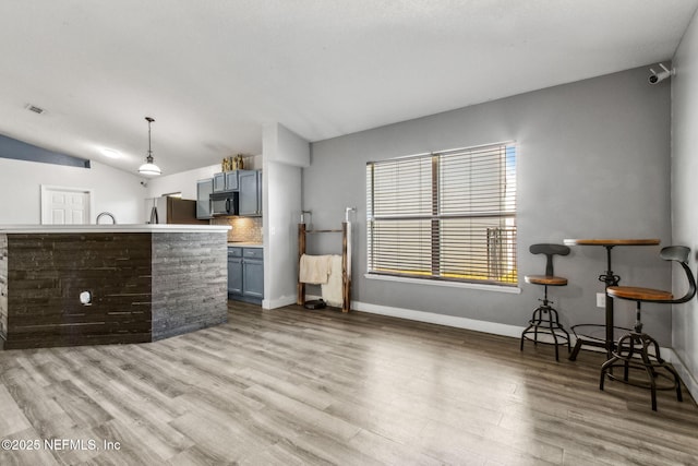 kitchen with decorative backsplash, black microwave, light wood-style floors, vaulted ceiling, and freestanding refrigerator