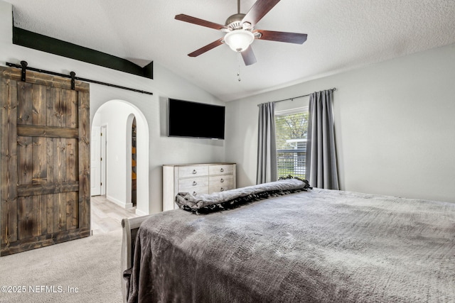 carpeted bedroom featuring a textured ceiling, ceiling fan, arched walkways, lofted ceiling, and a barn door