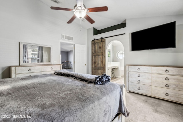 bedroom featuring arched walkways, a barn door, visible vents, light carpet, and ensuite bathroom