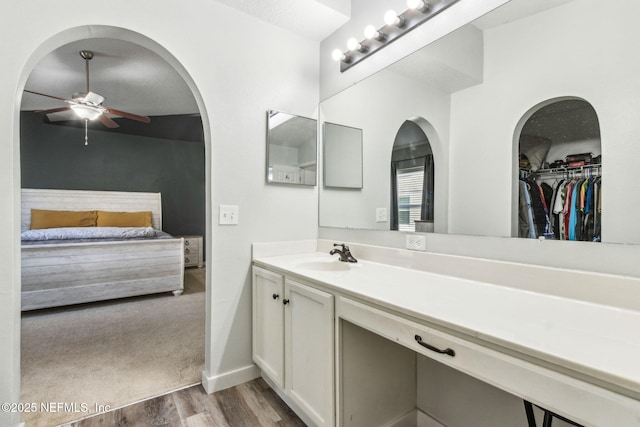 bathroom featuring baseboards, ceiling fan, wood finished floors, vanity, and ensuite bath
