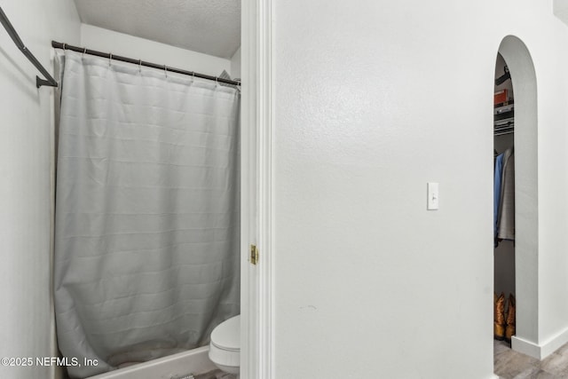 bathroom with baseboards, toilet, curtained shower, and a textured ceiling