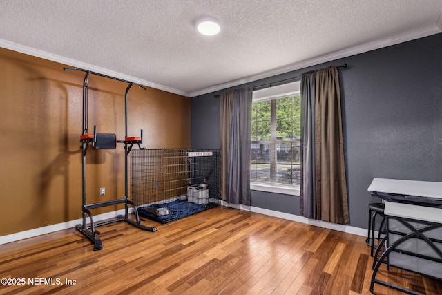 workout area featuring a textured ceiling, crown molding, baseboards, wood finished floors, and a textured wall