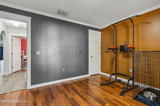 workout room with ornamental molding, wood finished floors, arched walkways, and visible vents