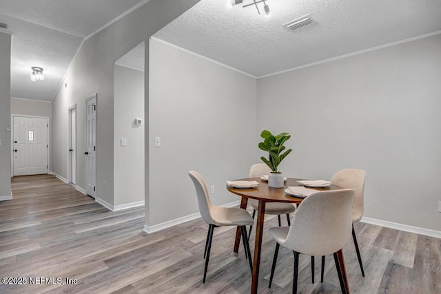 dining area featuring light wood-style floors, baseboards, visible vents, and a textured ceiling