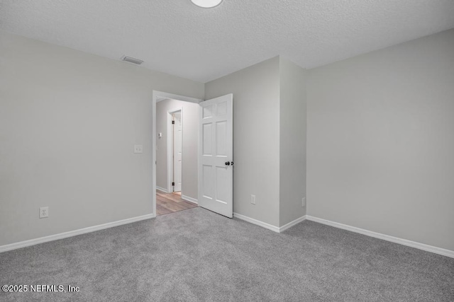 carpeted empty room featuring a textured ceiling, baseboards, and visible vents