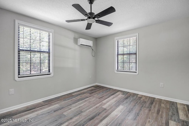 unfurnished room with a textured ceiling, wood finished floors, baseboards, and an AC wall unit