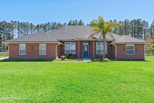 view of front of home featuring brick siding, fence, roof with shingles, and a front lawn