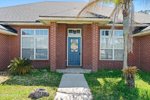 entrance to property featuring brick siding and a shingled roof