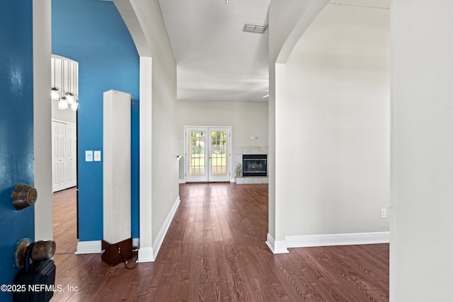 hall featuring baseboards, visible vents, wood finished floors, and arched walkways