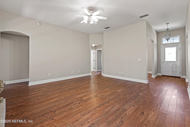 unfurnished living room with dark wood-style flooring, baseboards, arched walkways, ceiling fan, and visible vents