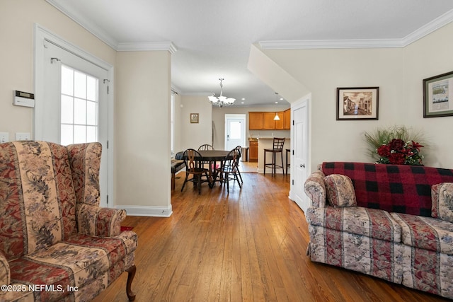 living room featuring baseboards, a chandelier, crown molding, and wood-type flooring