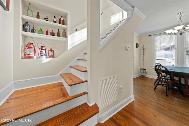 staircase with visible vents, baseboards, ornamental molding, wood finished floors, and an inviting chandelier