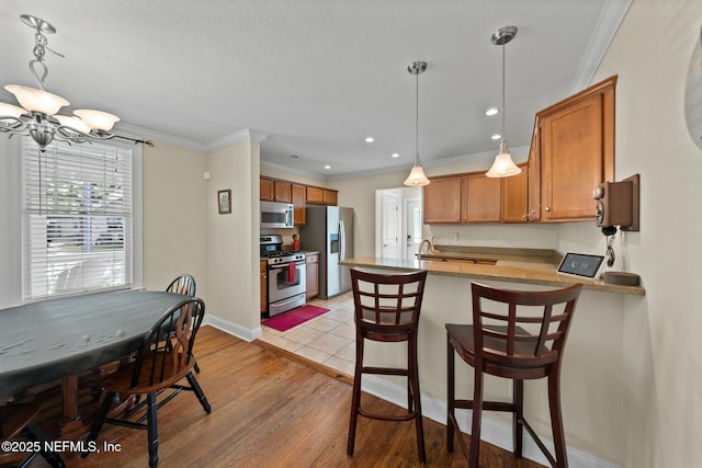 kitchen with a chandelier, appliances with stainless steel finishes, a peninsula, brown cabinetry, and ornamental molding