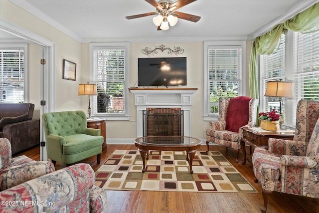 sitting room with a brick fireplace, crown molding, baseboards, a ceiling fan, and wood finished floors