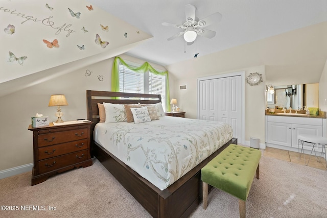 bedroom featuring a closet, baseboards, light carpet, ensuite bath, and vaulted ceiling