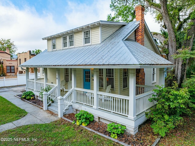 view of front facade featuring a porch, metal roof, fence, and a chimney