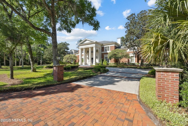 greek revival inspired property featuring a chimney, stucco siding, decorative driveway, and a front yard