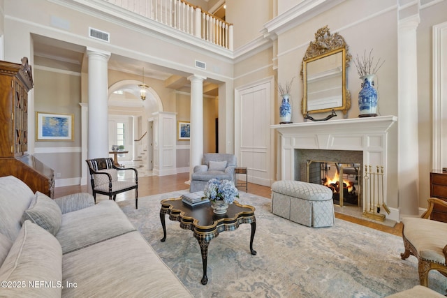 living area with a fireplace, ornate columns, wood finished floors, and visible vents