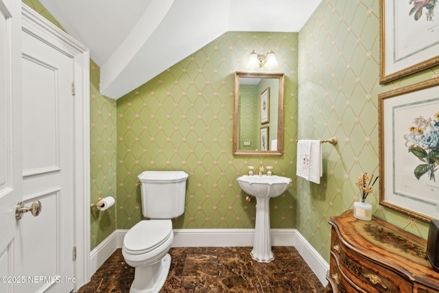 half bath with toilet, baseboards, vaulted ceiling, and marble finish floor