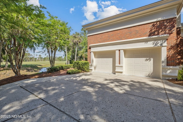 view of side of home featuring brick siding, a garage, and concrete driveway