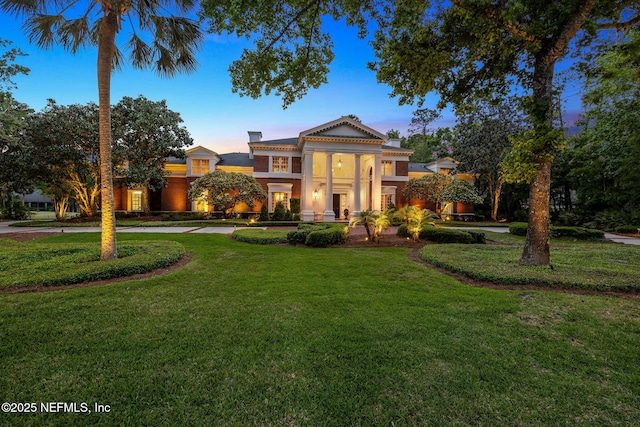 neoclassical home featuring stucco siding, a yard, and a chimney