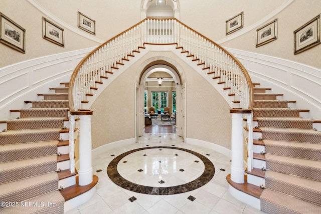 foyer entrance featuring stairs, arched walkways, a decorative wall, and a towering ceiling