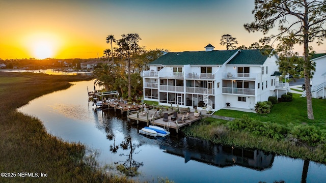 3387 Lighthouse Point Ln, Jacksonville, FL 32250 - back of house at dusk featuring a sunroom, a yard, a water view, a balcony, and a shingled roof
