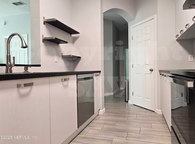 kitchen with wood finish floors, open shelves, visible vents, arched walkways, and stove