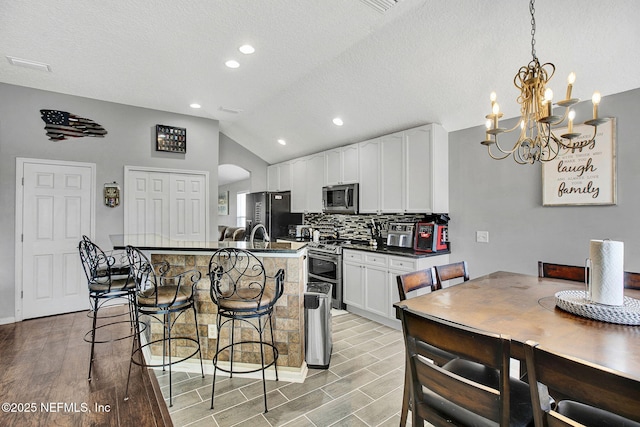 kitchen with a breakfast bar area, lofted ceiling, stainless steel appliances, dark countertops, and an inviting chandelier