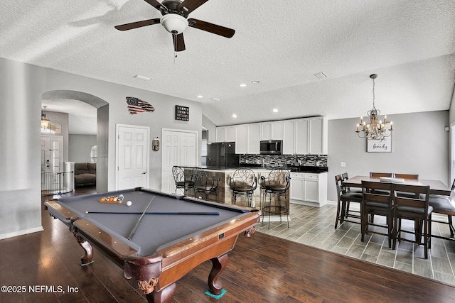 game room featuring vaulted ceiling, ceiling fan with notable chandelier, arched walkways, light wood-style flooring, and billiards