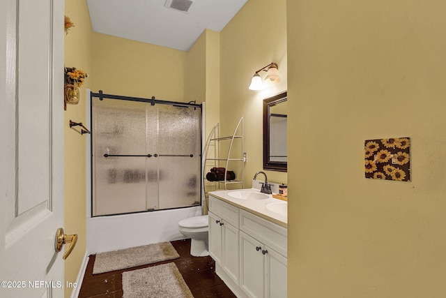 bathroom with visible vents, double vanity, combined bath / shower with glass door, toilet, and a sink