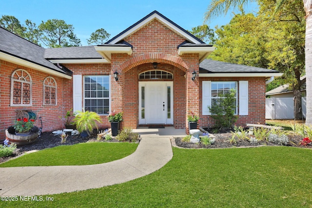 entrance to property with a lawn, brick siding, and a shingled roof
