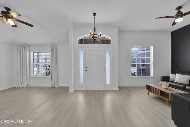foyer entrance featuring ceiling fan with notable chandelier, light wood-style floors, baseboards, and a textured ceiling