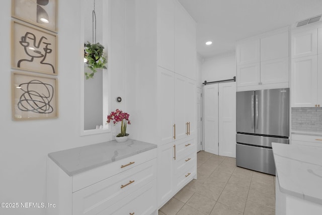kitchen featuring freestanding refrigerator, a barn door, tasteful backsplash, visible vents, and white cabinets