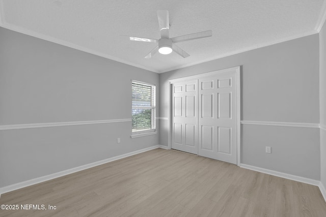 unfurnished bedroom with crown molding, a closet, wood finished floors, a textured ceiling, and baseboards