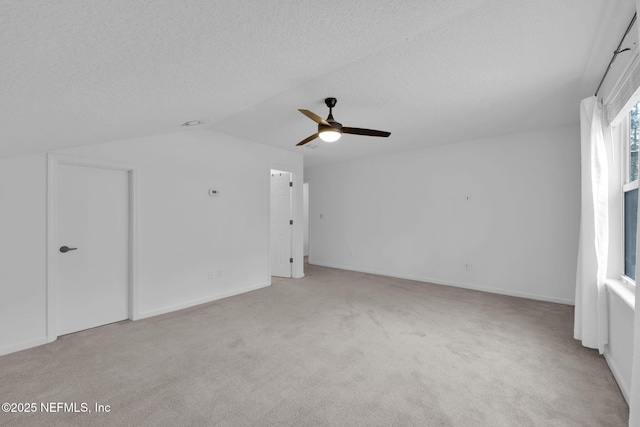 interior space featuring vaulted ceiling, baseboards, a textured ceiling, a ceiling fan, and light carpet