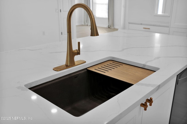 details featuring white cabinetry, a sink, backsplash, and light stone counters