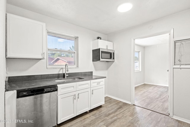 3838 Winton Dr, Jacksonville, FL 32208 - kitchen with stainless steel appliances, a sink, dark countertops, light wood finished floors, and white cabinets