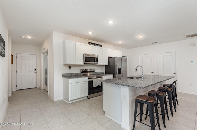 kitchen with a kitchen bar, an island with sink, a sink, stainless steel appliances, and baseboards