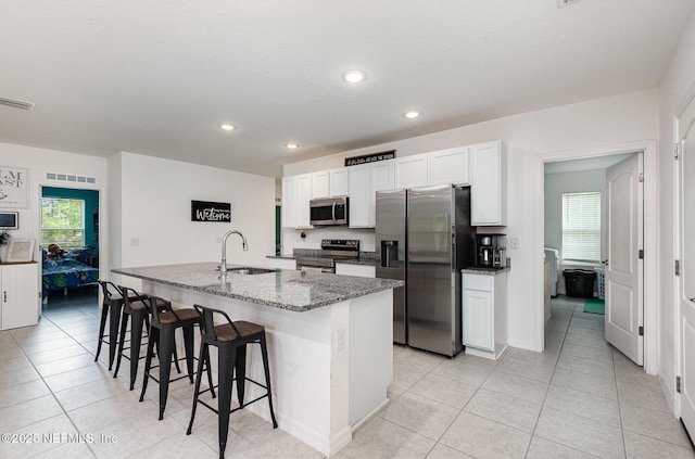 kitchen featuring a breakfast bar, a sink, white cabinets, a center island with sink, and appliances with stainless steel finishes
