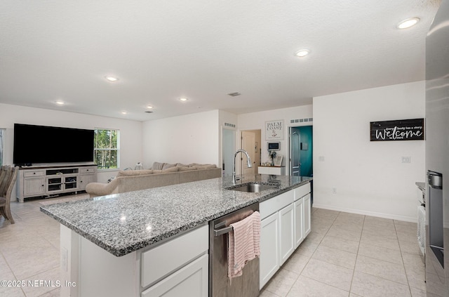 kitchen with a sink, white cabinets, a center island with sink, stainless steel dishwasher, and light stone counters