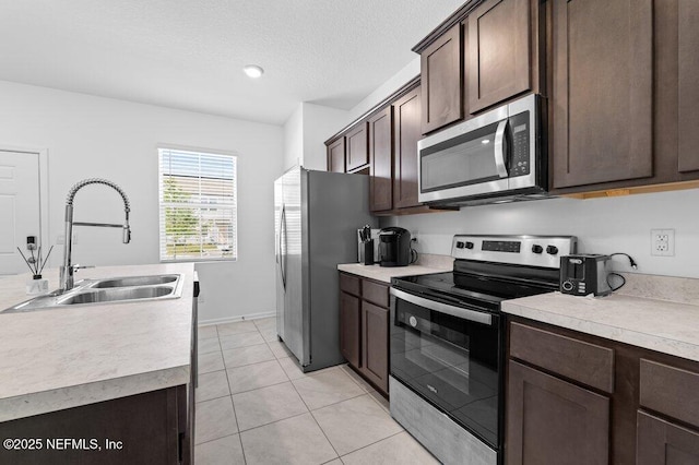 kitchen featuring a textured ceiling, light countertops, stainless steel appliances, dark brown cabinets, and a sink