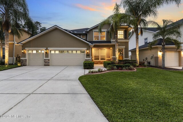 view of front of house with stucco siding, a yard, driveway, stone siding, and an attached garage