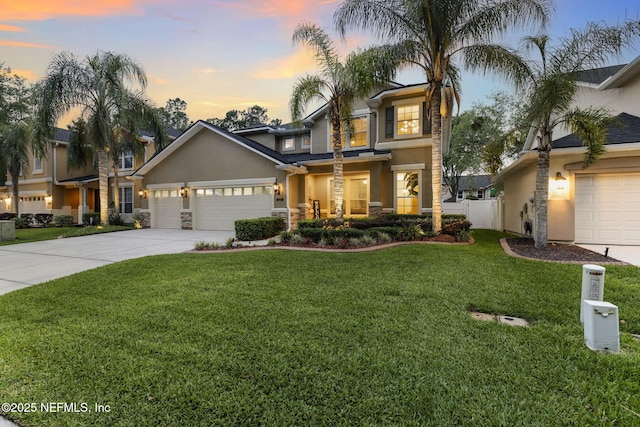 traditional home featuring stucco siding, a yard, driveway, stone siding, and an attached garage
