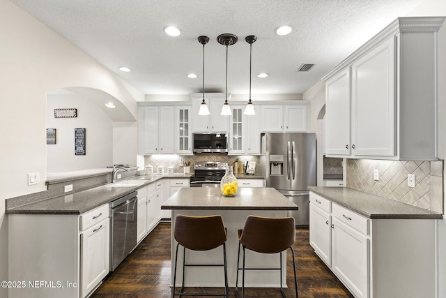 kitchen featuring glass insert cabinets, a sink, appliances with stainless steel finishes, visible vents, and arched walkways