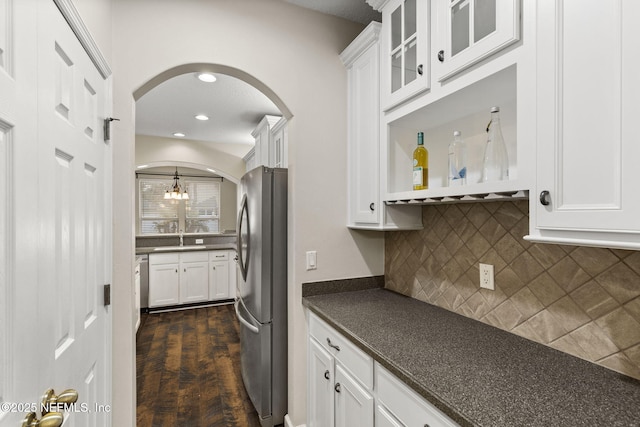 kitchen featuring white cabinetry, dark countertops, freestanding refrigerator, and arched walkways