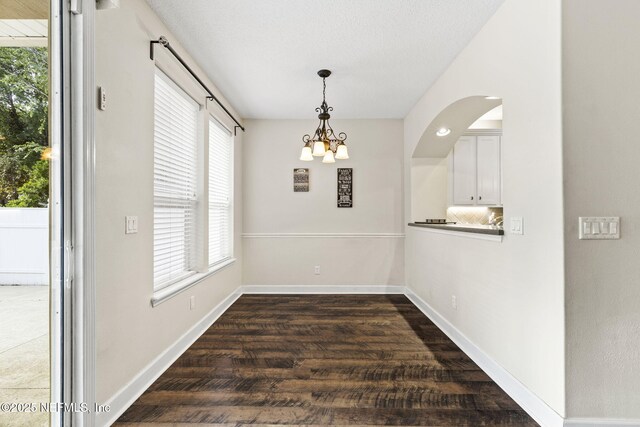 unfurnished dining area featuring baseboards, a chandelier, and dark wood finished floors