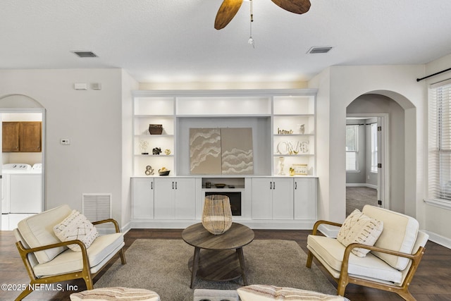 living room with washer and clothes dryer, a ceiling fan, visible vents, baseboards, and arched walkways